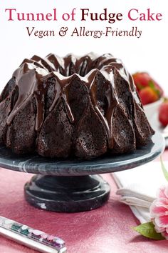 a bundt cake with chocolate icing on a plate next to strawberries and flowers