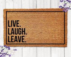 a door mat with the words live laugh leave on it next to purple and white flowers