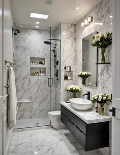 a bathroom with marble walls and flooring, white flowers in vases on the sink