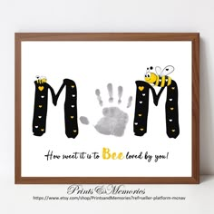 a hand print with the words mom and two bees on it, in front of a white wall