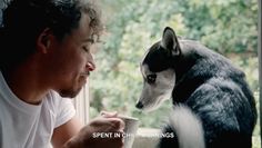 a man sitting next to a black and white dog drinking out of a coffee cup