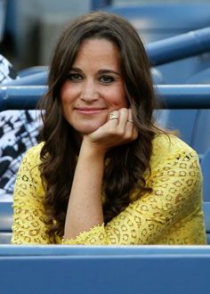 a woman sitting in the stands at a tennis game wearing a yellow dress and diamond ring