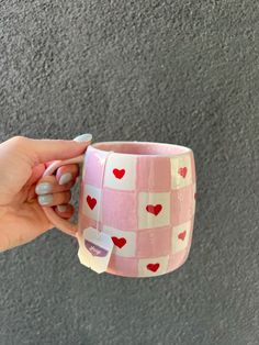 a person holding a pink and white coffee cup with hearts on the inside, in front of a gray background