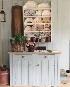 a cabinet with plates and cups on it in a room that has blue walls, wood floors and white paneling