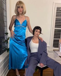 two women in blue dresses posing for the camera with one woman sitting on a chair