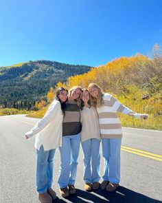 three girls are standing on the side of the road in front of a mountain range