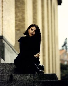 a woman sitting on top of a stone step next to a tall building with columns