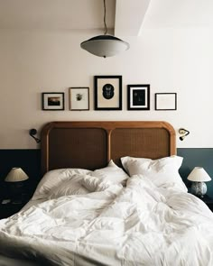 an unmade bed with white sheets and pictures on the wall above it in a bedroom