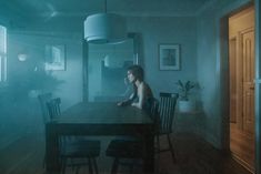 a woman sitting at a table in the middle of a room with blue light coming from behind her