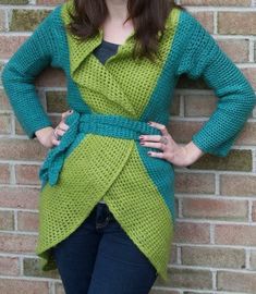 a woman standing in front of a brick wall wearing a green and blue cardigan