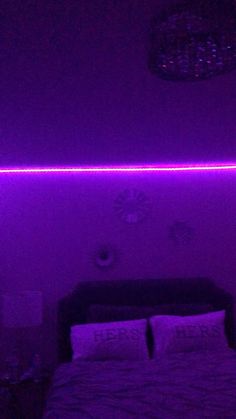 a bed in a room with purple lights on the wall and pillows under it,