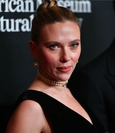 a woman in a black dress with a high bun and pearls on her head, posing for the camera