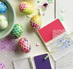 an assortment of colorfully painted eggs and notebooks on a white surface with confetti sprinkles