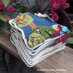 a stack of crocheted blankets sitting on top of a wooden bench next to flowers