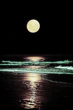 the moon is shining brightly over the water at night on the beach with waves coming in