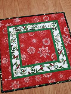 a red and white quilted placemat with green border on wooden floor next to table