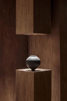 a black vase sitting on top of a wooden block in the middle of a room