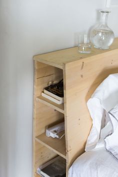 a bed with white sheets and pillows next to a wooden shelf filled with books on top of it