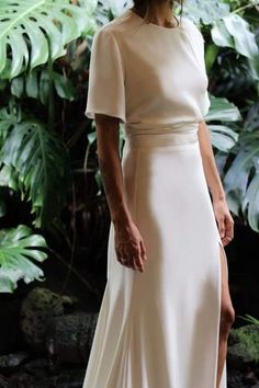 a woman in a white dress standing next to plants