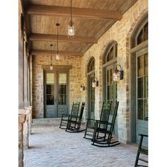 three rocking chairs on the front porch of a house with stone pillars and doors leading to another room