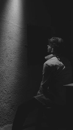 black and white photograph of man sitting on bench in dark room with light coming through window