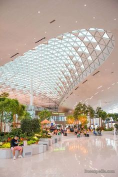 people are sitting on benches in the middle of an airport lobby with large glass ceiling