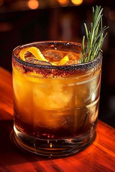 a close up of a drink on a table with a sprig of rosemary