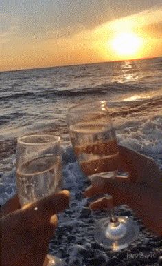 two people holding wine glasses in front of the ocean at sunset or sunrise on a boat