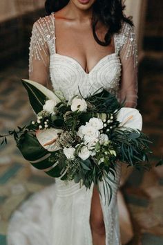 a woman in a wedding dress holding a bouquet with greenery and flowers on it