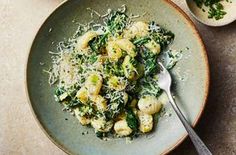 a bowl filled with pasta and spinach covered in parmesan cheese on top of a table