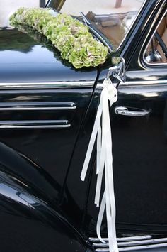 an old black car with white ribbons tied to it