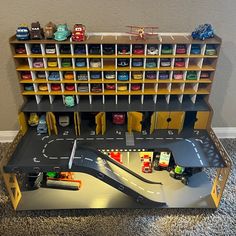 a toy race track with cars and trucks on it in front of a bookshelf