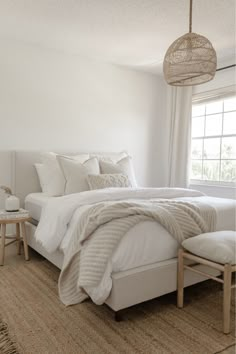 a bedroom with white linens and neutral colors is pictured in this image, there are two chairs at the foot of the bed