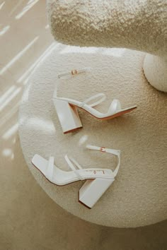 two pairs of white high heeled shoes sitting on top of a round table next to a towel