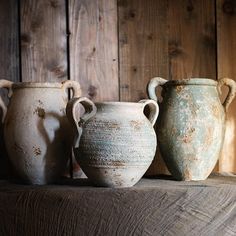 three old vases sitting on top of a wooden shelf in front of a wood wall