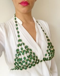 a woman wearing a white shirt and green beaded necklace on her left shoulder, looking at the camera