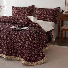 a bedroom with a bed covered in maroon bedspread and matching comforter set