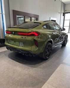 the rear end of a green bmw suv in a showroom with large windows and doors