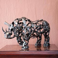 a sculpture of a rhino made out of metal circles on a wooden table against a pink wall