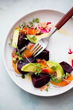 a white plate topped with assorted veggies next to a knife and fork