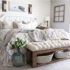 a bed with white sheets and pillows in a bedroom next to a table with baskets on it