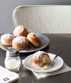 powdered sugar covered donuts on plates next to salt and pepper shakers