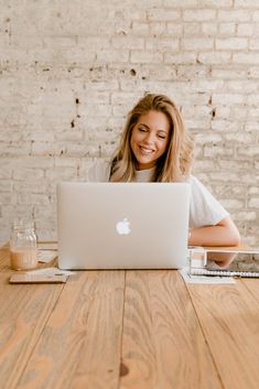 a woman sitting at a table with an apple laptop in front of her, smiling