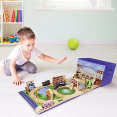 a little boy playing with a toy train set on the floor next to a green ball