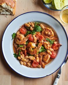 a white plate topped with shrimp and beans next to a slice of bread on top of a wooden table