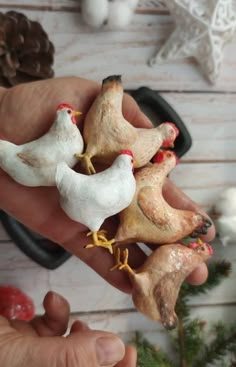 small chicken figurines are held in the palm of someone's hand with pine cones