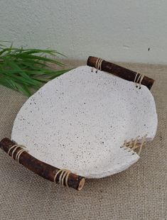 a white plate with two brown handles and some bamboo sticks on the rim, sitting next to a green plant