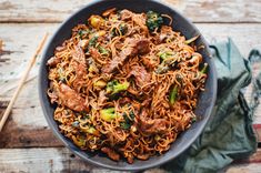 a bowl filled with noodles and meat on top of a wooden table next to chopsticks