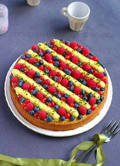 a cake decorated with raspberries and blueberries on a plate next to silverware