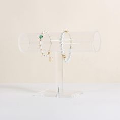 two bracelets are on display in a clear glass holder, one is green and the other is white